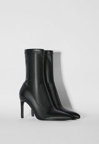 Svarta läder ankelstövlar med spetsiga tår, smala högklackar och dekorativ sömnad. Slät yta och åtsittande design.