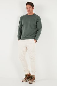 Felpa grigio chiaro a maniche lunghe, abbinata a pantaloni jogger color avorio e sneakers con dettagli marroni e un design testurizzato.