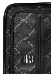 Intérieur de valise en tissu noir avec poche en maille, fermetures éclair et motif de logo "WITTCHEN". Comprend une étiquette d'entretien en noir, rouge et blanc.