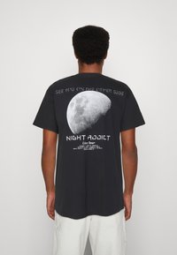 Schwarzes Baumwoll-T-Shirt mit einer großen Mondgrafik auf dem Rücken, mit dem Text "SEE YOU ON THE OTHER SIDE" und "NIGHT ADDICT" darunter.