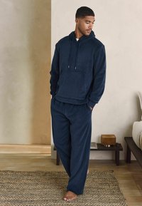 Completo da loungewear in pile morbido di colore blu navy, con top con cappuccio dotato di tasca frontale e pantaloni abbinati a vestibilità ampia. Tessuto a trama, design casual.