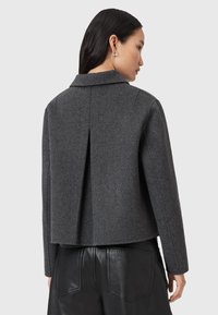 Veste en mélange de laine grise avec un col pointu, un détail de pli au dos et une coupe courte. Associée à un pantalon en cuir taille haute.