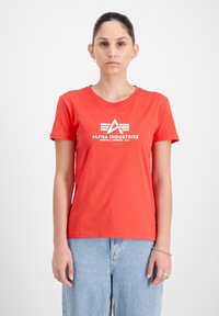 Raudona medvilninė marškinė su apvaliu kaklu ir trumparankoviais, su baltu spaudiniu "ALPHA INDUSTRIES" priekyje.