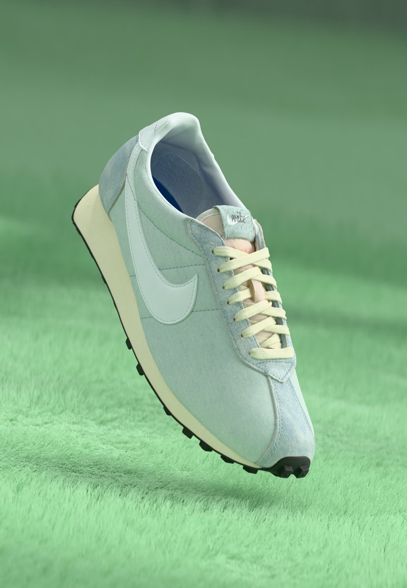 Sapatilha Nike azul claro com atacadores e sola creme, flutuando acima de uma superfície verde texturizada.