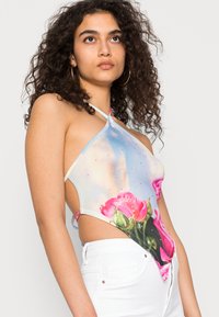 Top halter floral com fundo de céu azul, apresentando rosas cor-de-rosa, tecido transparente e pequenos cristais. Combinado com calças brancas de cintura alta.