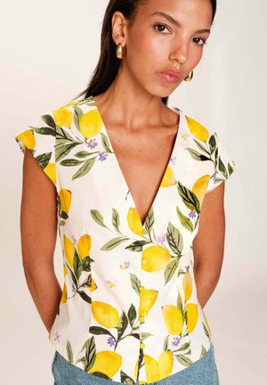 Blouse blanche à manches courtes avec un imprimé citron et floral, dotée d'un décolleté en V et de boutons jaunes à l'avant. Texture de tissu lisse.