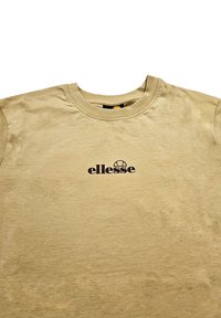 Camiseta de manga corta beige hecha de tela suave, con cuello redondo y el logo negro "ellesse" impreso en la parte frontal.