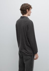 Mørkegrå langærmet poloshirt med klassisk krave, lavet af blødt tekstureret stof. Kombineret med sorte denimjeans, set bagfra.