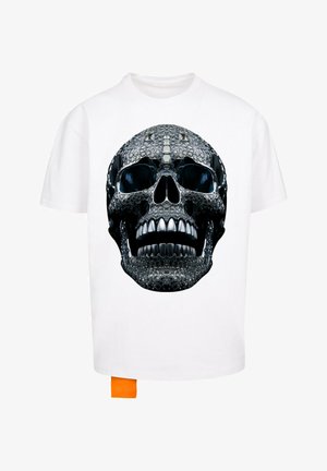 Balta marškinėliai su dideliu juodu kaukolės grafiku, blizgiais akcentais, tekstūruotais detalėmis ir koralinė etiketė apatiniame kairiajame kampe.