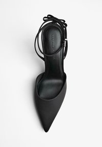Scarpa con tacco alto in satin nero, con punta affusolata, apertura sul retro e sottile cinturino alla caviglia legato a fiocco, caratterizzata da un interno liscio e lucido.