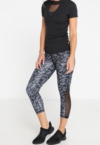 Svart kortärmad skjorta med nätparti, kombinerad med gråmönstrade caprileggings med svarta nätpaneler på sidorna och svarta sportskor.