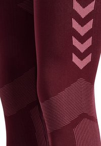 Nærbillede af mørkerøde leggings med lyserøde chevron- og stribede mønstre på knæ og lår.