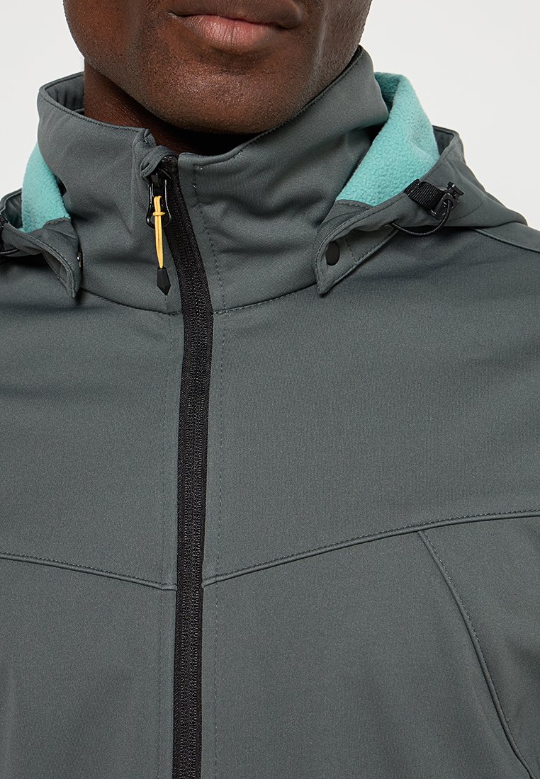 Veste grise avec un col haut, dotée d'une doublure en polaire turquoise, d'une fermeture éclair noire et de cordons réglables sur la capuche. Texture de tissu lisse.