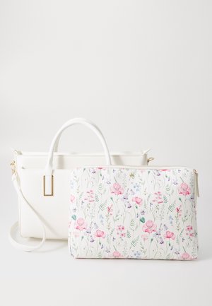 Sac à main en cuir blanc avec poignées courtes et bandoulière amovible, posé à côté d'une pochette blanche zippée à motif floral rose et violet.