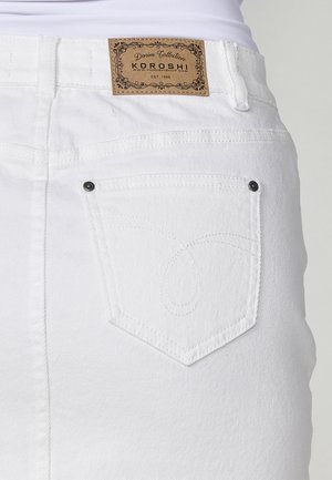Weiße Jeansrock mit einem Lederetikett, auf dem "KOROSHI" steht, kontrastierenden Nähten und einer einzigartigen Form der Gesäßtasche mit schwarzen Nieten.