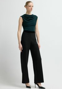 Top in zeegroen met een gestructureerde afwerking, gecombineerd met zwarte, wijde, high-waist broekspijpen en zwarte, puntige hakken. Eenvoudig, elegant ontwerp.