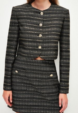 Woman wearing a black and white striped buttoned jacket and matching high-waisted skirt with buttoned pockets.