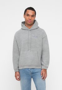 Sweat à capuche gris en tissu doux avec une poche frontale, un cordon de serrage à la capuche et un logo brodé bleu sur la poitrine. Coupe décontractée et manches longues.