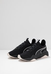 Zwarte sportschoenen met een gestructureerde bovenkant, contrasterende witte accenten, ronde neus en gevoerde kraag. Rubberen zool met een geribbeld patroon.