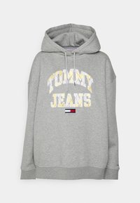Šedá mikina s kapucí se znakem "TOMMY JEANS" v žluté a bílé barvě, s malým trojbarevným emblémem dole a žebrovanými manžetami.