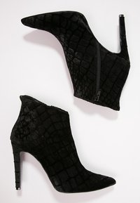 Botines de tacón alto negros, hechos de terciopelo texturizado con un patrón de cocodrilo y detalle de cremallera lateral, con punta afilada y tacón de aguja.