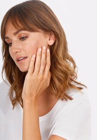 Anello d'argento con una pietra preziosa a forma di pera, indossato su una mano appoggiata sul viso. Design semplice, con una fascia liscia e una pietra trasparente.