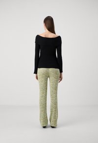 Svart ribbad off-shoulder topp i kombination med gröna texturerade utsvängda byxor med flerfärgade mönster. Modell vänder ryggen mot kameran.