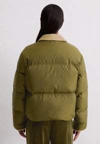 Olivgrüne Pufferjacke mit einem plüschigen beigen Kragen, im boxy Schnitt und mit gesteppter Textur. Die Rückansicht zeigt eine eng anliegende Passform und gestickte Details.