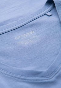 T-shirt di cotone azzurro chiaro con scollo a V, caratterizzato da dettagli del marchio e del materiale stampati in bianco, texture liscia e cuciture rinforzate.