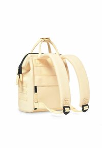 Cream backpack with black zipper, featuring adjustable straps. Made of durable fabric, it includes exterior pockets and unique strap design.