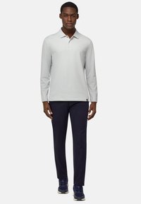 Lichtgrijze langärmige polo, met klassieke kraag, gecombineerd met marineblauwe broek en donkere sneakers. Glad stof, aansluitend ontwerp.