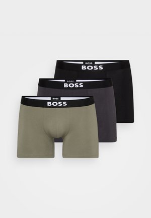 Tre paia di boxer in cotone: verde oliva, grigio scuro e nero. Ognuno presenta un elastico nero con la scritta "BOSS" stampata in bianco. Texture del tessuto liscia.