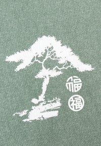 Vihreä kangas, jossa on valkoinen kuvio puusta tyyliteltyine oksineen, kuvion alapuolella kaksi pyöreää symbolia teksteineen.