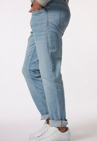 Vaaleansiniset farkut, joissa on kapeneva malli, käänteetlahkeissa ja etutaskut. Yhdistettynä valkoisiin tennareihin ja harmaaseen neuleeseen.