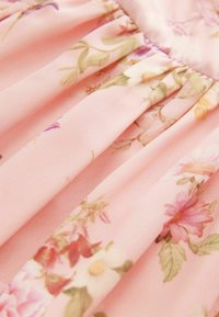 Tela de color rosa claro con patrones florales en colores lavanda, púrpura y rosa; presenta una textura suave y fruncidos para dar volumen.