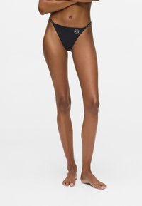 Zwarte stringbikini met smalle zijbandjes, minimale bedekking en een klein logodetail aan de voorkant. Gladde stoftextuur.