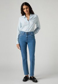 Camicia azzurro chiaro a maniche lunghe con bottoni, jeans blu a vita alta e mocassini neri. I jeans presentano tasche frontali e un design a gamba dritta.