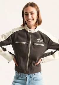 Kurtka VANS z dwukolorowym wzorem, z ciemnym korpusem i kremowymi rękawami, zapinana na zamek, z kieszeniami na zamek i wysokim kołnierzem. Wykonana z teksturowanej tkaniny.