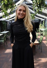 Czarna bluzka z długim rękawem ozdobiona błyszczącymi drobinkami, z wysokim kołnierzem, zestawiona z lejącą się czarną spódnicą. Gładka faktura, dopasowane gorsety i luźna talia.