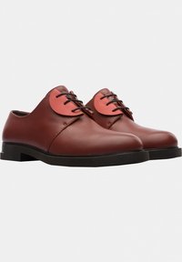 Braune Lederschuhe mit runder Spitze, die an der Oberseite einen roten Akzent und schwarze Schnürsenkel aufweisen. Flache schwarze Sohle für Stabilität.