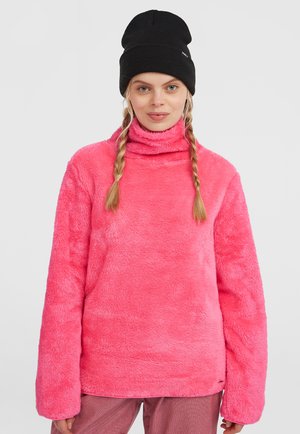Suéter de pelo sintético rosa con cuello alto, mangas largas y una textura suave. El diseño presenta un ajuste holgado y se combina con un gorro negro.