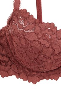 Soutien-gorge en dentelle dans une couleur rose douce, avec des motifs floraux, un recouvrement en dentelle texturée et des bretelles réglables. Bords festonnés à l'ourlet.