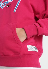 Felpa di cotone fucsia con tasca frontale, maniche a costine e etichetta del marchio cucita all'orlo. Logo blu audace sul petto.
