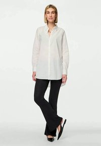 Camisa branca de botões com mangas longas, combinada com calças pretas de flare com textura canelada e sapatos pretos de bico fino. Sem padrões ou texturas notáveis.