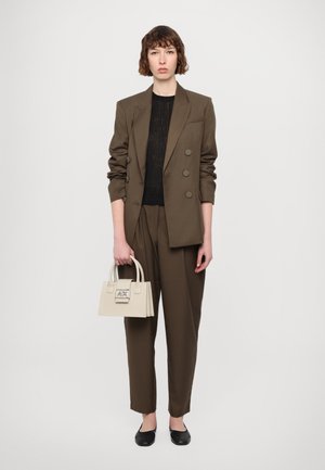 Bruine op maat gemaakte blazer met dubbele knopen, zwart gestructureerd topje, losse bruine broek en een kleine crèmekleurige handtas met een logo. Zwarte flats.