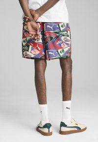 Pantaloni corti colorati con un motivo misto di vari loghi e numeri, principalmente rosso, verde e blu. Indossati con calze bianche e scarpe da ginnastica multicolori.