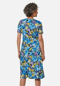 Blumenkleid mit einem Muster aus Blau, Gelb und Lila. Kurzärmlig, knielang und aus einem weichen Stoff mit tailliertem Schnitt.