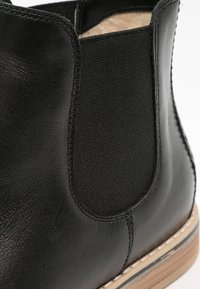 Gros plan sur une botte Chelsea en cuir noir avec un panneau latéral élastique et un bord de semelle en bois.