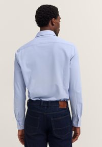 Helles blaues Langarmhemd mit normalem Kragen, Knopfmanschetten und glatter Textur, kombiniert mit dunkelblauen Jeans aus Denim mit aufgesetzten Taschen.