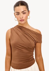 Bruine top met één schouder in een zachte, rekbare stof met geplooide details aan de zijkant. Glad textuur, aansluitend ontwerp.